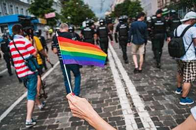 Person waving rainbow flag at pride with police in background